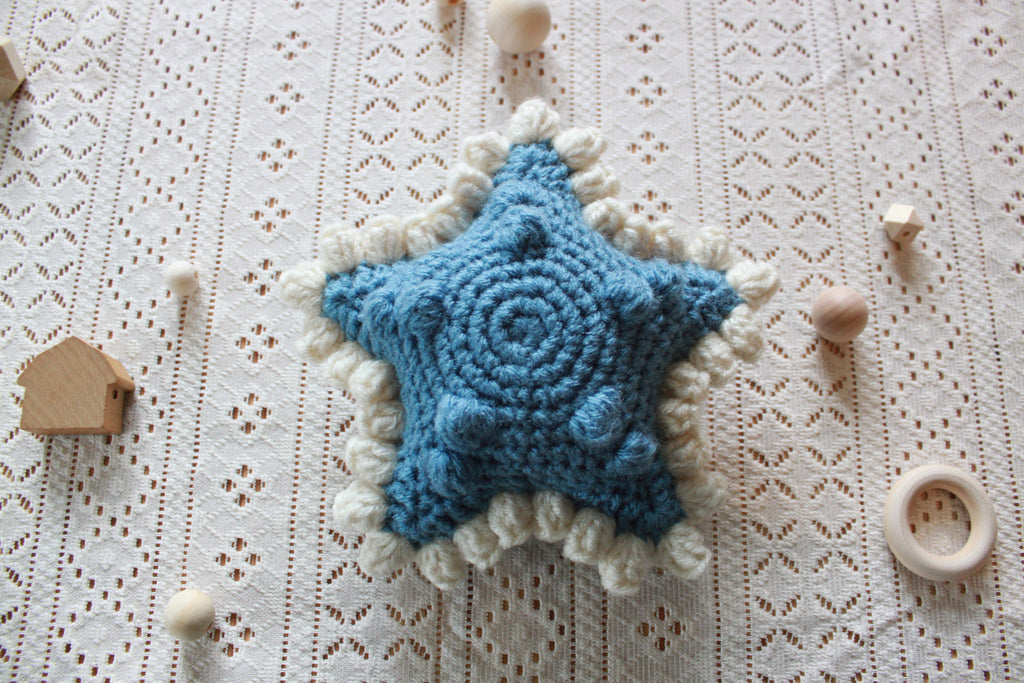 Blue crochet star baby rattle with white accents on a textured surface. Pdf pattern tutorial